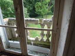 Fenêtre du deuxième étage sans vitre et balcon endommagé.